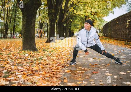 Donna atletica in forma che fa esercizio prima di fare jogging nel parco cittadino autunnale sul parco giochi per bambini. Giovane fitness femminile runner che allunga le gambe mentre wa Foto Stock