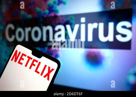 Un logo Netflix visualizzato su un telefono cellulare con un modello illustrativo del Coronavirus visualizzato su un monitor in background. Foto Stock
