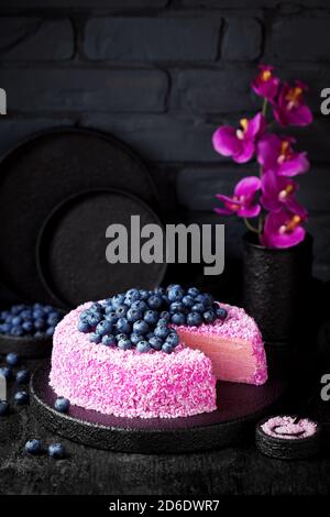 Torta crepe fatta in casa con panna pitahaya rosa al cocco e mirtilli freschi su sfondo nero, fuoco selettivo Foto Stock