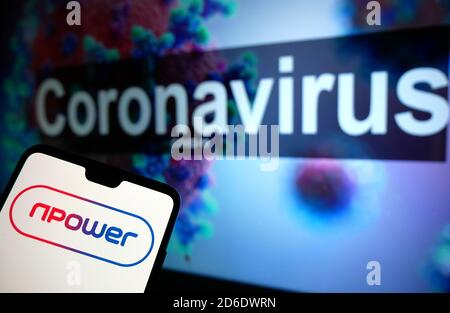 Il logo npower visualizzato su un telefono cellulare con un modello illustrativo del Coronavirus visualizzato su un monitor sullo sfondo. Foto Stock