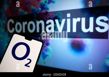 Il logo O2 visualizzato su un telefono cellulare con un modello illustrativo del Coronavirus visualizzato su un monitor sullo sfondo. Foto Stock