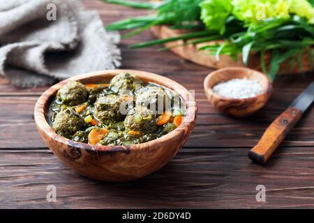 Zuppa con polpette, verdure ed erbe in ciotola di legno, fuoco selettivo Foto Stock