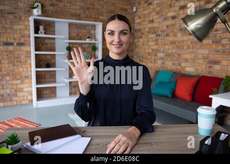Ritratto di giovane donna che agita la mano mentre si siede la sua scrivania Foto Stock