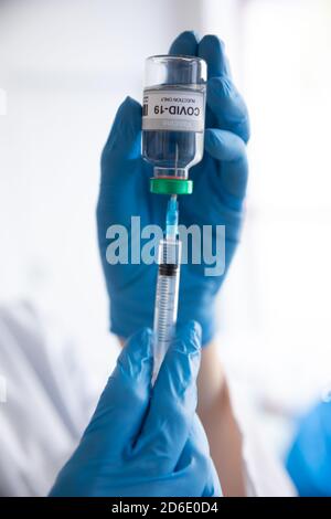 Primo piano del medico che inietta la siringa in un flacone Con testo Covid-19 Foto Stock