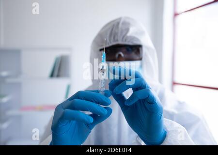 Operatore sanitario che indossa indumenti protettivi che tengono una siringa Foto Stock