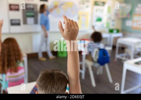 Studenti che alzano le mani in classe a scuola Foto Stock