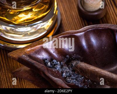 Bicchiere di whisky sulle rocce e un sigaro che brucia in un posacenere Foto Stock