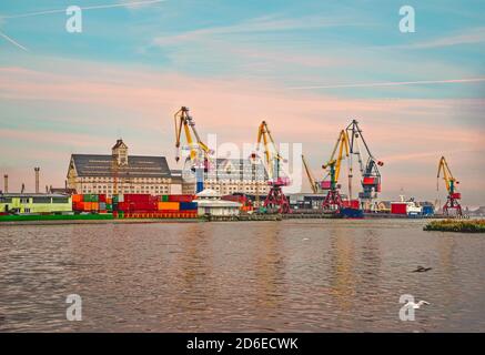 Vista sul porto marittimo di Kaliningrad con gru. Fiume Pregol al tramonto. Gru per carico pesante sul porto. Deposito cargo. Scena industriale Foto Stock