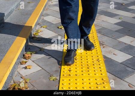 Uomo che cammina su blocchi gialli di pavimentazione tattile per ciechi handicap.blocchi di Braille, piastrelle tattili per ipovedenti, Tenji Blocks.Textured Foto Stock