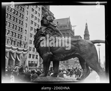 Il fotografo Frederick O. Bemm è seduto sulla cima di una statua di leone di fronte all'Art Institute of Chicago durante una parata, Chicago, Illinois, 1910. Foto Stock