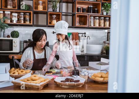 Madre e figlia asiatiche godono di fare e decorare ciambelle in cucina vita reale, concetto di cucina di famiglia Foto Stock