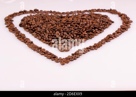 Chicchi di caffè arrostiti disposti a forma di cuore su sfondo chiaro. Cuore con un bordo. Foto Stock