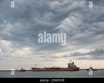 la petroliera chimica entra nel porto con i rimorchiatori, sotto un cielo tempestoso Foto Stock