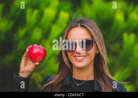 Donna vegana sorridente che mostra una mela rossa gustosa su sfondo verde. Foto Stock