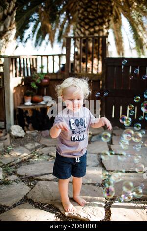 Ragazzo di due anni in piedi in Yard giocando con le bolle Foto Stock