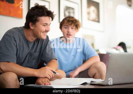 giovani maschi adulti che ridono e fanno i compiti in casa impostazione Foto Stock