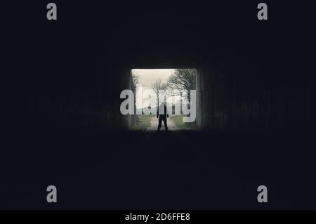 Una minacciosa figura incappucciata che si trova all'ingresso di a. lungo tunnel scuro Foto Stock