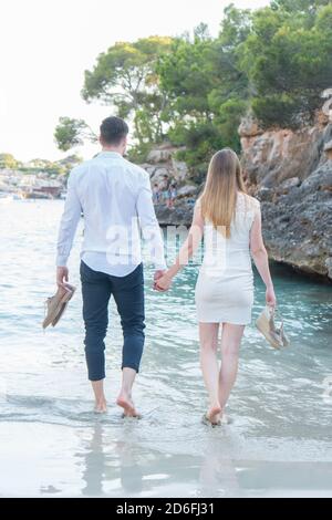 Scatto verticale di una coppia maschile e femminile che cammina romanticamente sul mare tenendo le mani Foto Stock