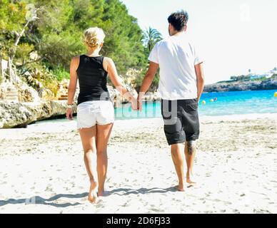 Coppia maschile e femminile romanticamente camminando sulla riva mentre tenere le mani Foto Stock
