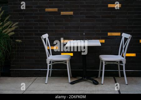 Un tavolo e sedie bianche per due persone sotto le regole di distanza sociale durante la pandemia di covid-19 a bar sul marciapiede