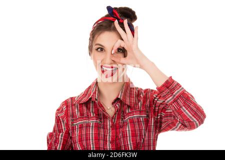 Immagine ravvicinata di giovane donna positiva con lunghi capelli scuri guardando la telecamera attraverso la mano nel gesto ok, mordere la propria lingua in eccitazione. Bella bru Foto Stock