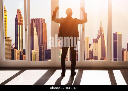 Uomo d'affari africano alzando le mani. Vista posteriore vicino alla finestra con il centro città Foto Stock