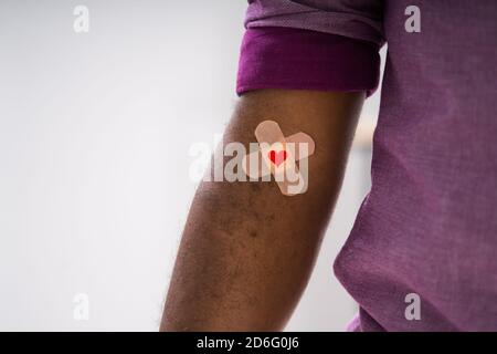 Concetto di donazione di sangue. Donatore afroamericano con aiuto di banda e cuore Foto Stock