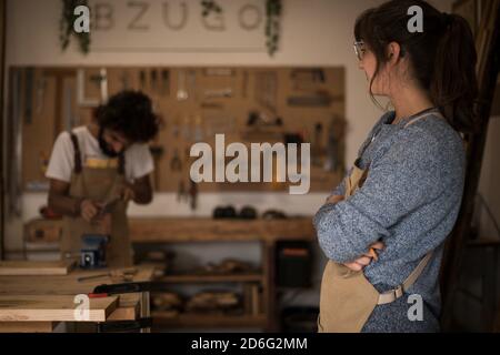 Giovane donna d'affari che lavora come falegname in una piccola officina di Falegnameria. Coppia di falegnami che lavorano insieme progettando il nuovo design di mobili per la casa. SM Foto Stock