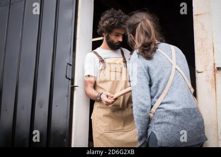 Una giovane coppia di falegnami che lavorano insieme in una piccola officina di carpenteria che progetta una nuova parte domestica di mobilia che si sta costruendo fuori del legno. Giovane entrpr Foto Stock