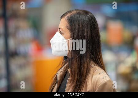 Donna in una maschera protettiva con un carrello durante una pandemia di coronavirus sta scegliendo il cibo nel negozio di alimentari. Foto Stock