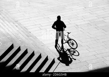 Belgrado, Serbia - 09 ottobre 2020: Sagoma d'ombra di una persona in piedi accanto a una bicicletta accanto alle scale esterne della città, da dietro in vista ad alto angolo Foto Stock