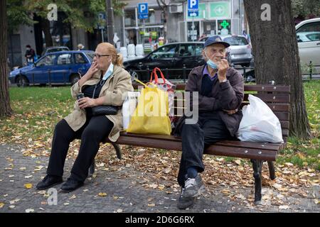 Belgrado, Serbia, 11 ottobre 2020: Donna seduta su una panchina fumando sigaretta accanto ad un uomo fumando pipa Foto Stock