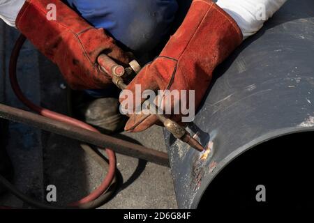 Saldatore che saldano un tubo largo di metallo con una torcia di taglio ossi-combustibile., primo piano dettaglio di mani e manico di torcia Foto Stock