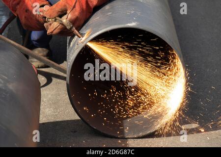 Saldatore che saldano un ampio tubo metallico con una torcia da taglio ad ossi-combustibile, con fiamma e scintille, in cantiere esterno Foto Stock