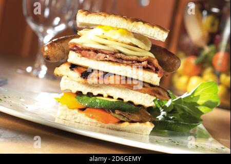 Sandwich con prosciutto, pancetta, uova fritte, formaggio, pomodori, lattuga, pane tostato e salsiccia Foto Stock