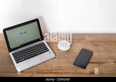 Adelaide, Australia - 7 luglio 2019: Google Home Mini con computer portatile HP con Windows 10 e telefono cellulare impostato sul tavolo accanto l'uno all'altro Foto Stock