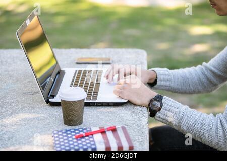 Giovane uomo che studia con il computer mentre ascolta la musica con cuffie nel parco senza maschera Foto Stock