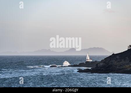 Una barca solitaria si allontana dalla Ria de Pontevedra in Galizia al tramonto, con le Isole Cies sullo sfondo. Foto Stock