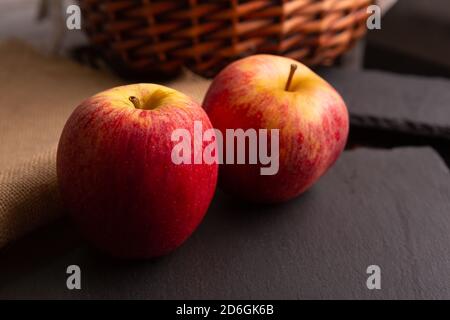 due mele rosse poste su un pezzo di ardesia dentro un ambiente poco luminoso Foto Stock