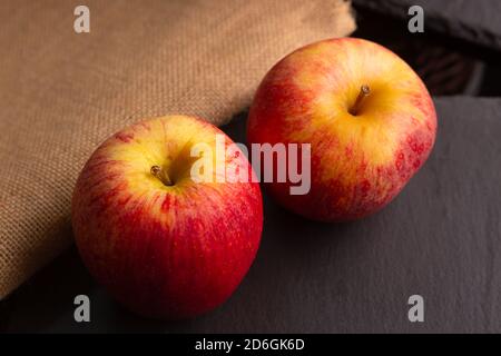 due mele rosse poste su un pezzo di ardesia dentro un ambiente poco luminoso Foto Stock