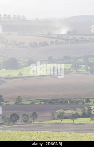 Trattori che arano campi in lontananza in un mosaico di campi agricoli nella campagna inglese nel Northumberland Foto Stock
