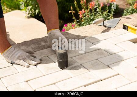 Il padrone stende le pietre di pavimentazione in strati. Percorso di pavimentazione di mattoni di giardino. Posa di lastre di pavimentazione in cemento nel cortile della casa su base di fondazione sabbia Foto Stock