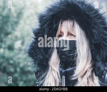 ritratto di una donna in un cappotto invernale con pelliccia cappuccio e maschera facciale per la protezione da virus Foto Stock