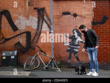 Nottingham, Nottinghamshire, Regno Unito. 17 ottobre 2020. Un uomo cammina il suo cane davanti a un pezzo di lavoro dell'artista dei graffiti Banksy. L'opera, all'esterno di un salone di bellezza, mostra una ragazza che si allena con un pneumatico di bicicletta accanto ad una bicicletta che manca la sua ruota posteriore. Credit Darren Staples/Alamy Live News. Foto Stock