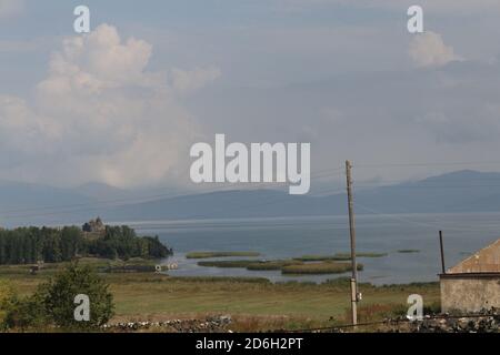 Riva erbosa di un piccolo villaggio vicino al lago di Sevan con Un monastero di Hayravank all'orizzonte Foto Stock