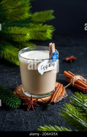 Bevanda calda di Natale. Eggnog con bastoncino alla cannella in vetro con rami Abete Tree su sfondo scuro. Foto Stock