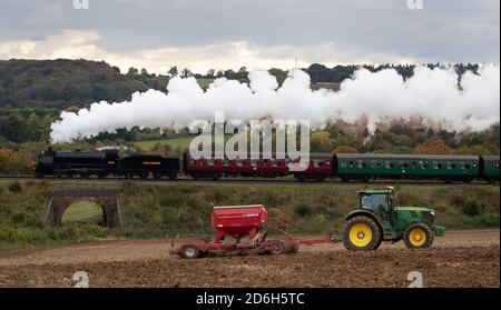 La locomotiva a vapore di classe S15 506 passa un trattore in un campo, mentre si trova lungo la Mid Hants Railway, conosciuta anche come la linea di Watercress, vicino a Rotley in Hampshire durante il fine settimana del gala a vapore d'autunno. Foto Stock