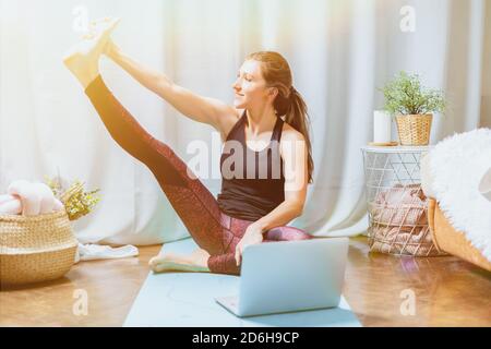 Giovane attraente donna sportiva che pratica yoga. Treni per sedersi sullo spago e stretching, allenarsi a casa in soggiorno. Sport e ricreazione con Foto Stock