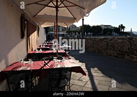 Vista di una piccola strada nel centro storico di Alghero con i tavoli di un ristorante in un soleggiato giorno Foto Stock