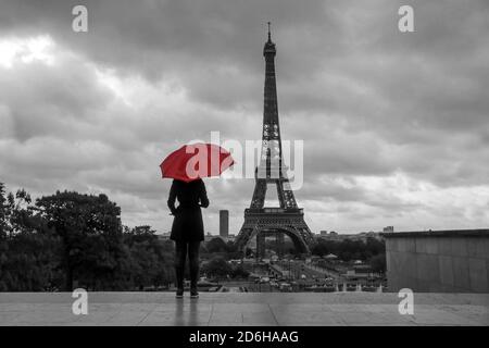 La signora con un ombrello rosso si trova di fronte alla Torre Eiffel a Parigi, in Francia. Immagine in bianco e nero con ombrello rosso isolato. Foto Stock